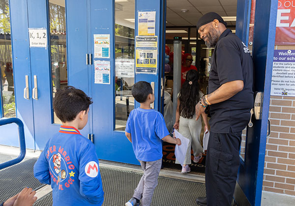 A group of students entering a school as a friendly school worker holds the door.