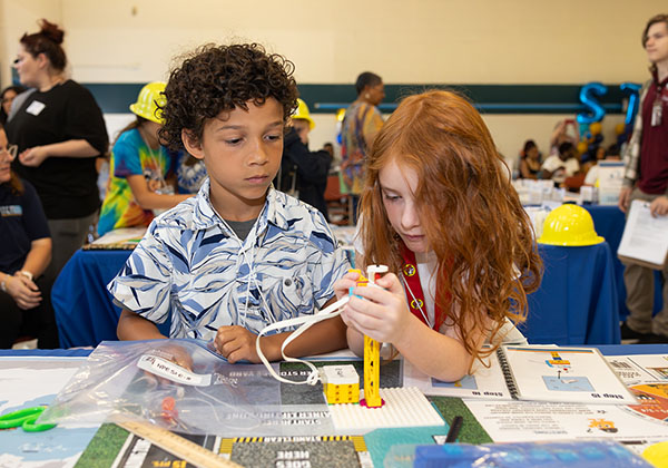 Two students focus on building a yellow crane model at the Engineering Design Challenge.