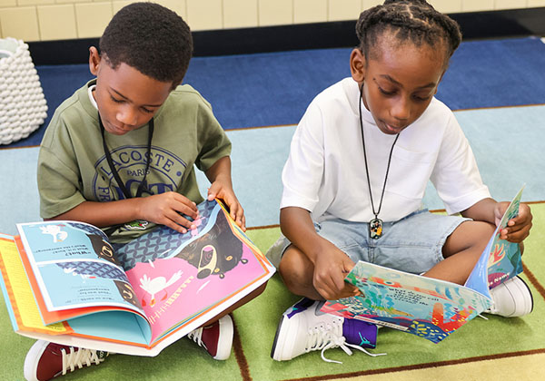 Two young NNPS students sitting on floor reading books