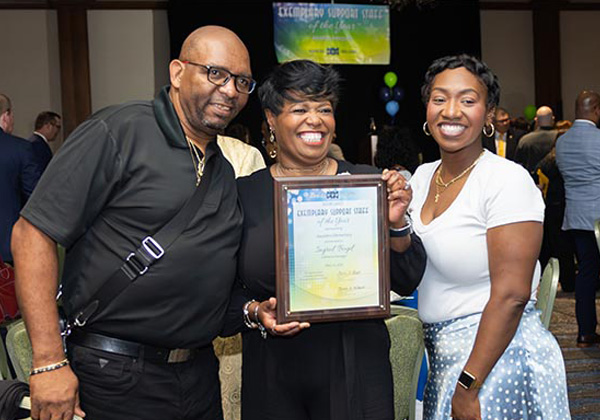 A beaming honoree poses with two guests holding her Exemplary Support Staff of the Year award plaque at the banquet.