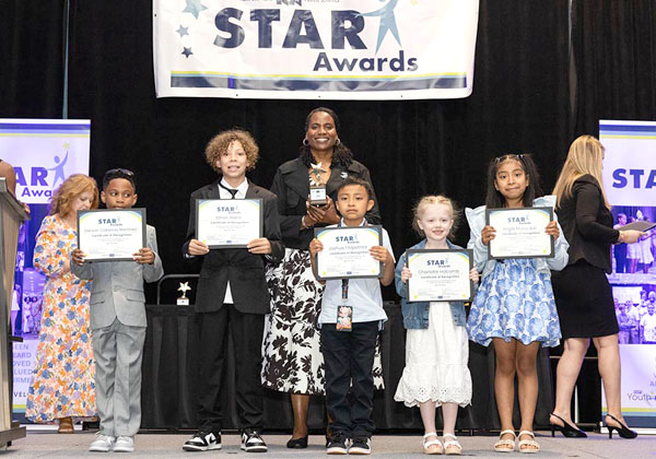 Children holding certificates on stage at STAR Awards with teacher behind them.