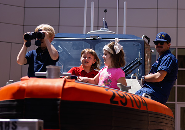 Children explore a U.S. Coast Guard boat display alongside an officer.
