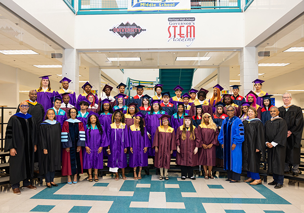 Graduating students and school staff pose for a group photo during a high school graduation ceremony.